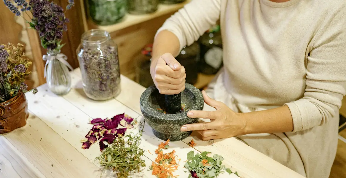 A woman using a mortar and pestle to prepare herbs in a rustic indoor setting.